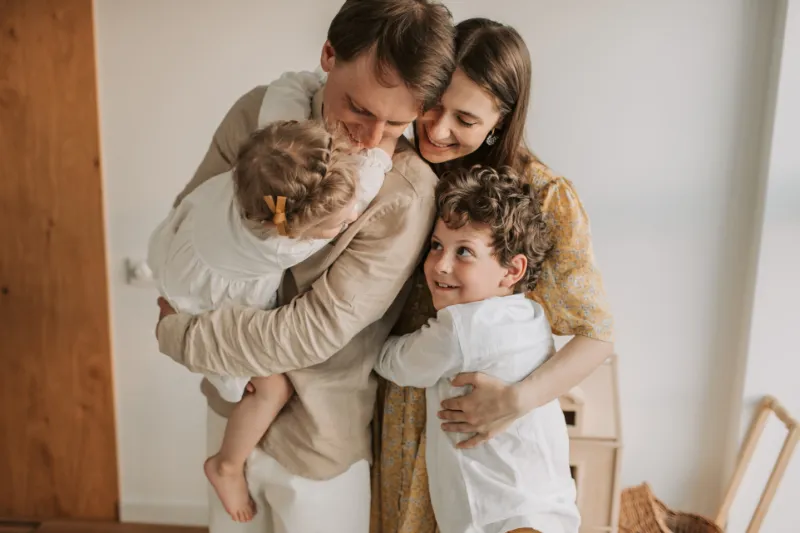 Pais e filhos em abraço carinhoso dentro de casa, representando segurança emocional e vínculos familiares fortalecidos.